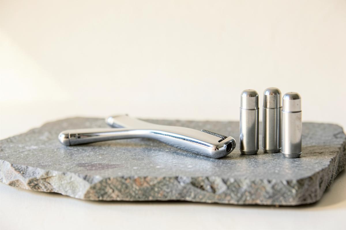 Chrome razor handle and three blade cartridges on a grey stone slab