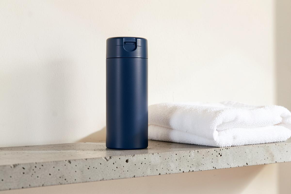 Dark blue deodorant can beside a folded white towel on a concrete shelf